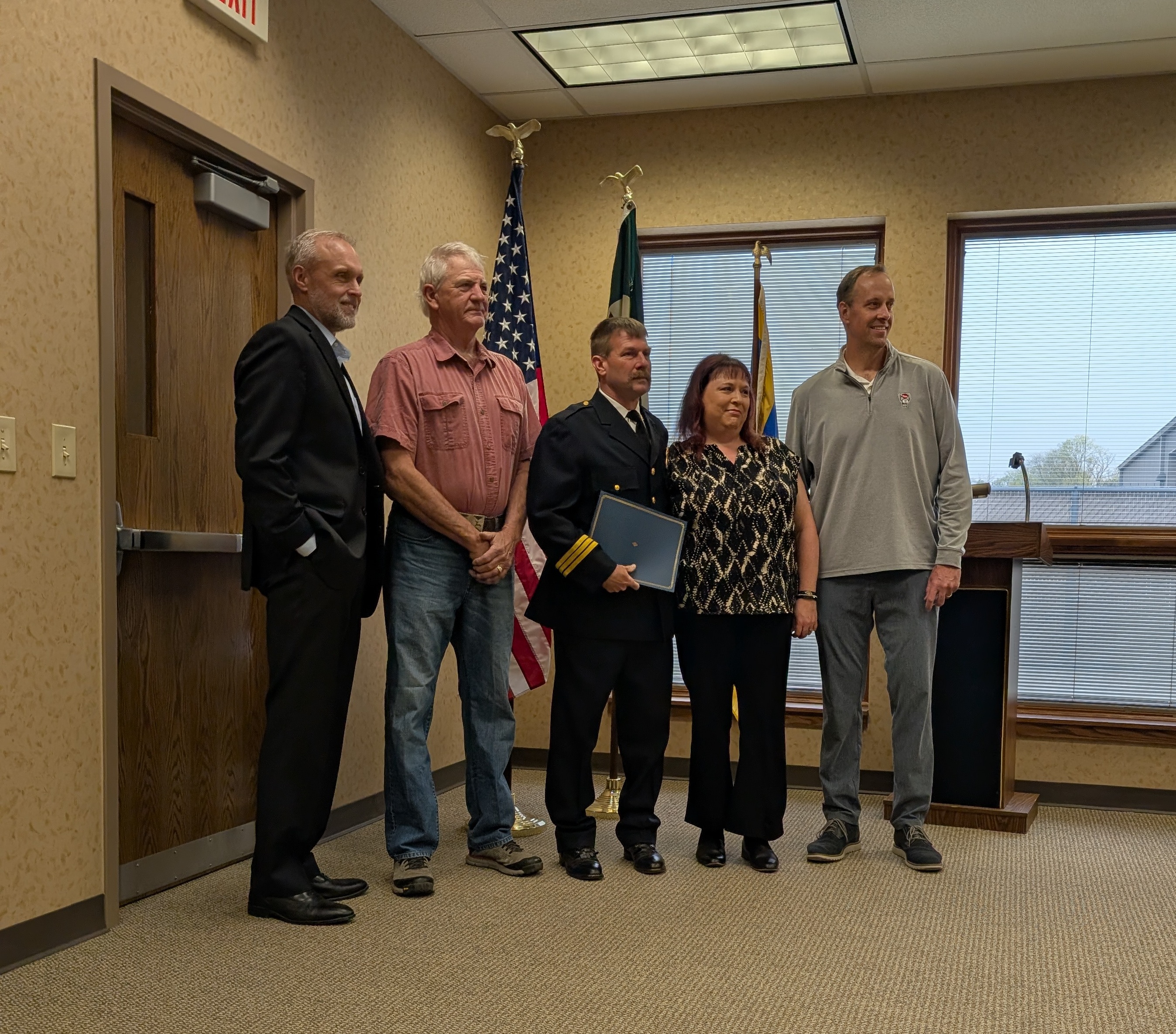 Image of 5 people standing in front of several flags and windows during a swearing in ceremony
